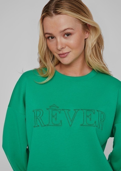 Eine Frau trägt einen grünen Pullover mit der Aufschrift "RÊVER".