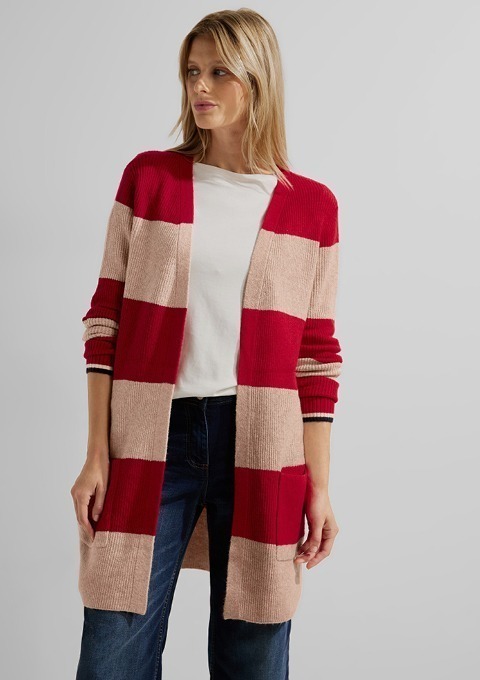 Eine Frau trägt eine gestreifte Strickjacke mit roten und beigen Streifen und ein weißes T-Shirt.