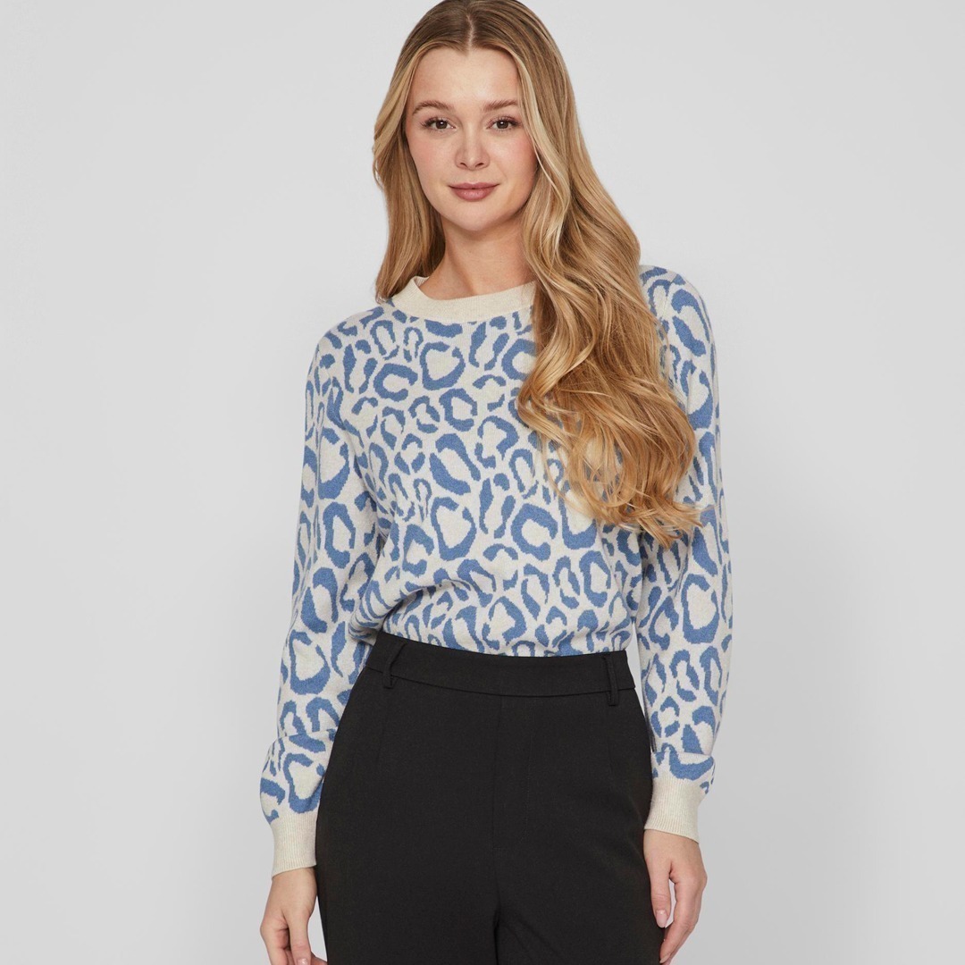 Eine Frau mit langen Haaren trägt einen blauen Pullover mit Leopardenmuster und schwarze Hose. Eine Frau mit langen Haaren trägt einen blauen Pullover mit Leopardenmuster und schwarze Hose.