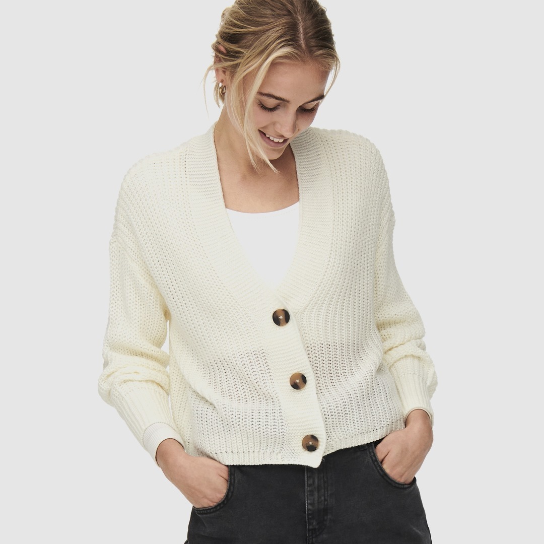 Eine Frau trägt einen weißen, gestrickten Cardigan mit Knöpfen, während sie lächelt.