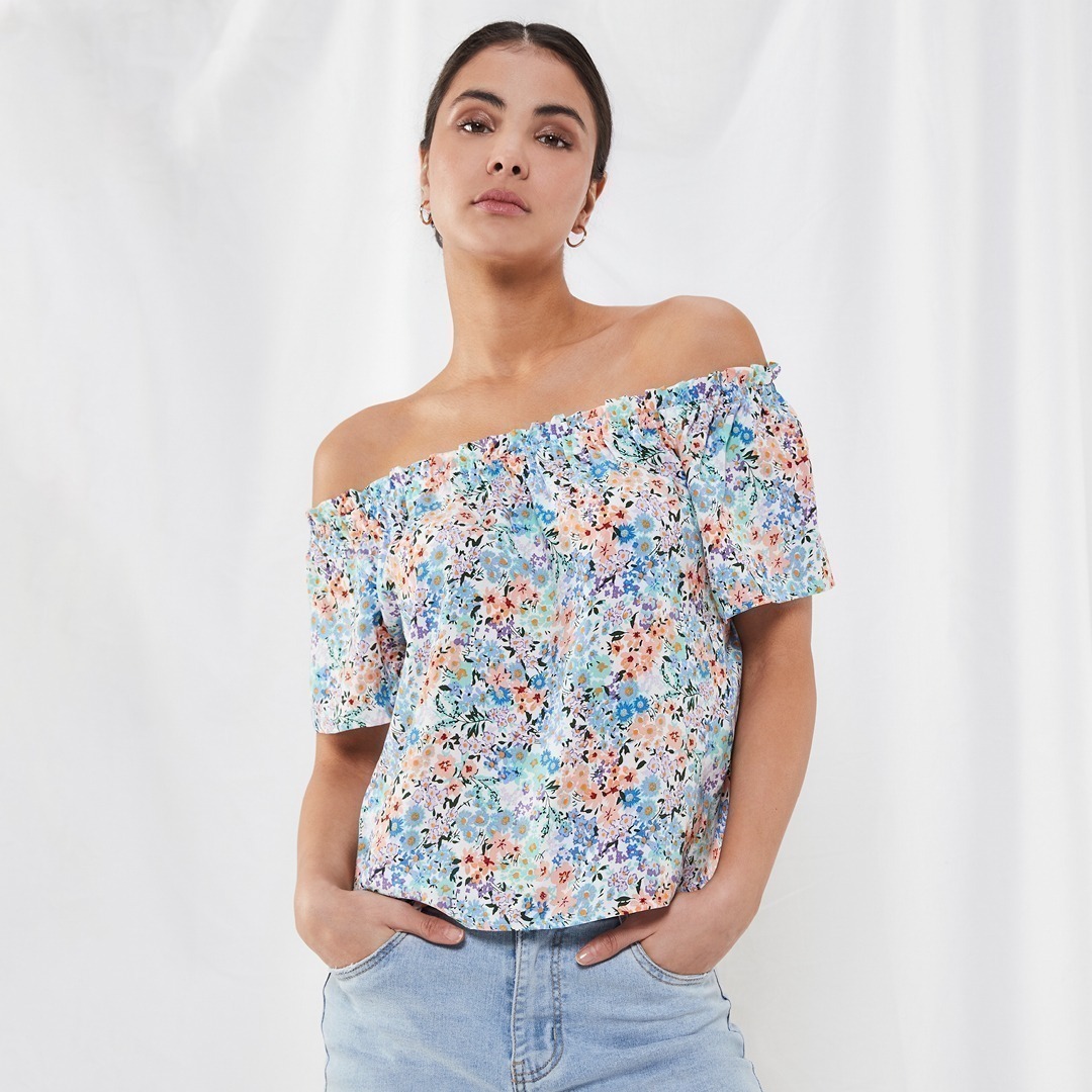 Eine Frau trägt ein buntes, blumenmuster Shirt mit schulterfreien Ärmeln und blauen Jeans. Eine Frau trägt ein buntes, blumenmuster Shirt mit schulterfreien Ärmeln und blauen Jeans.