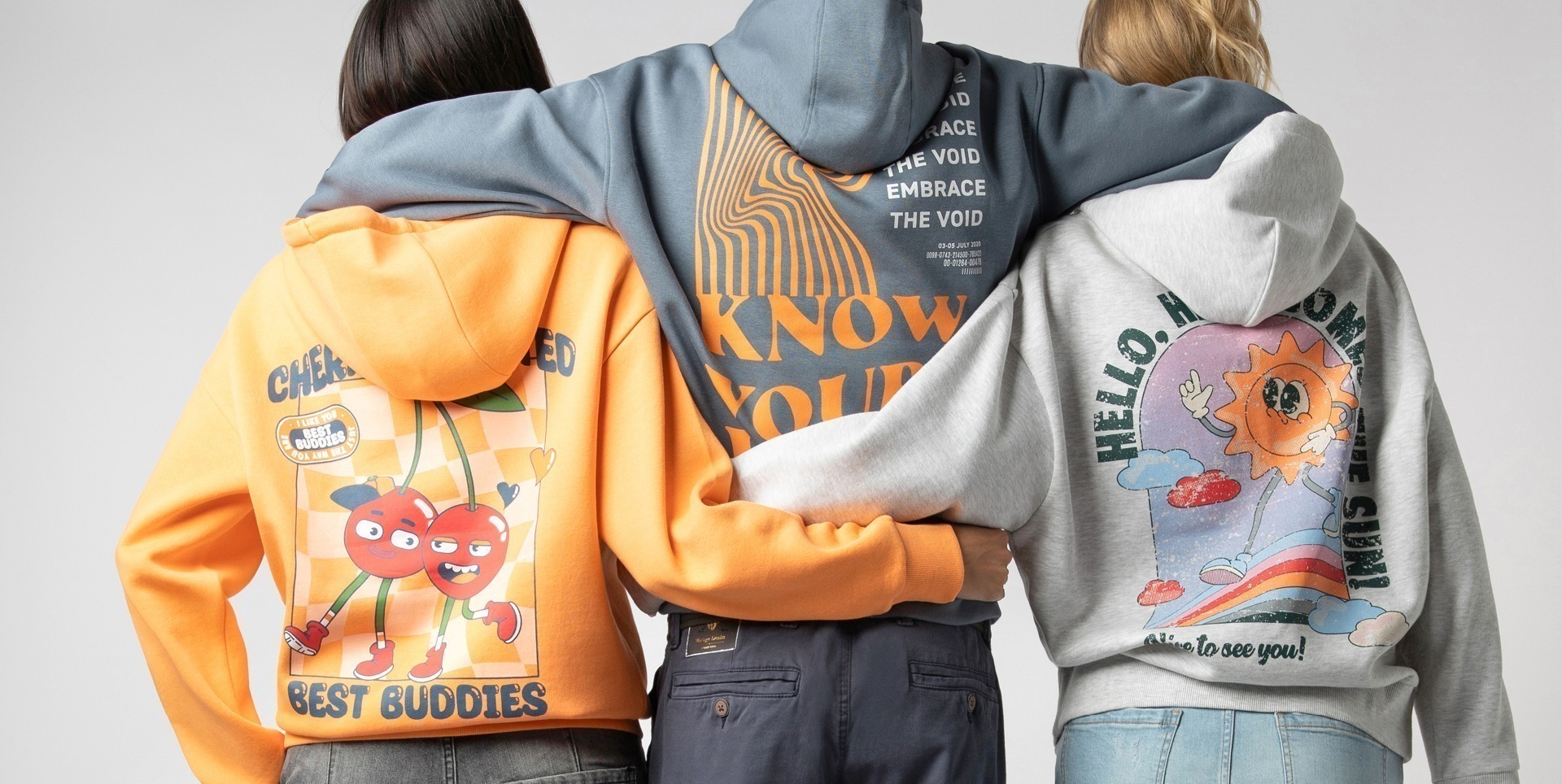 Drei Personen tragen farbige Kapuzenpullis mit verschiedenen grafischen Designs auf der Rückseite.