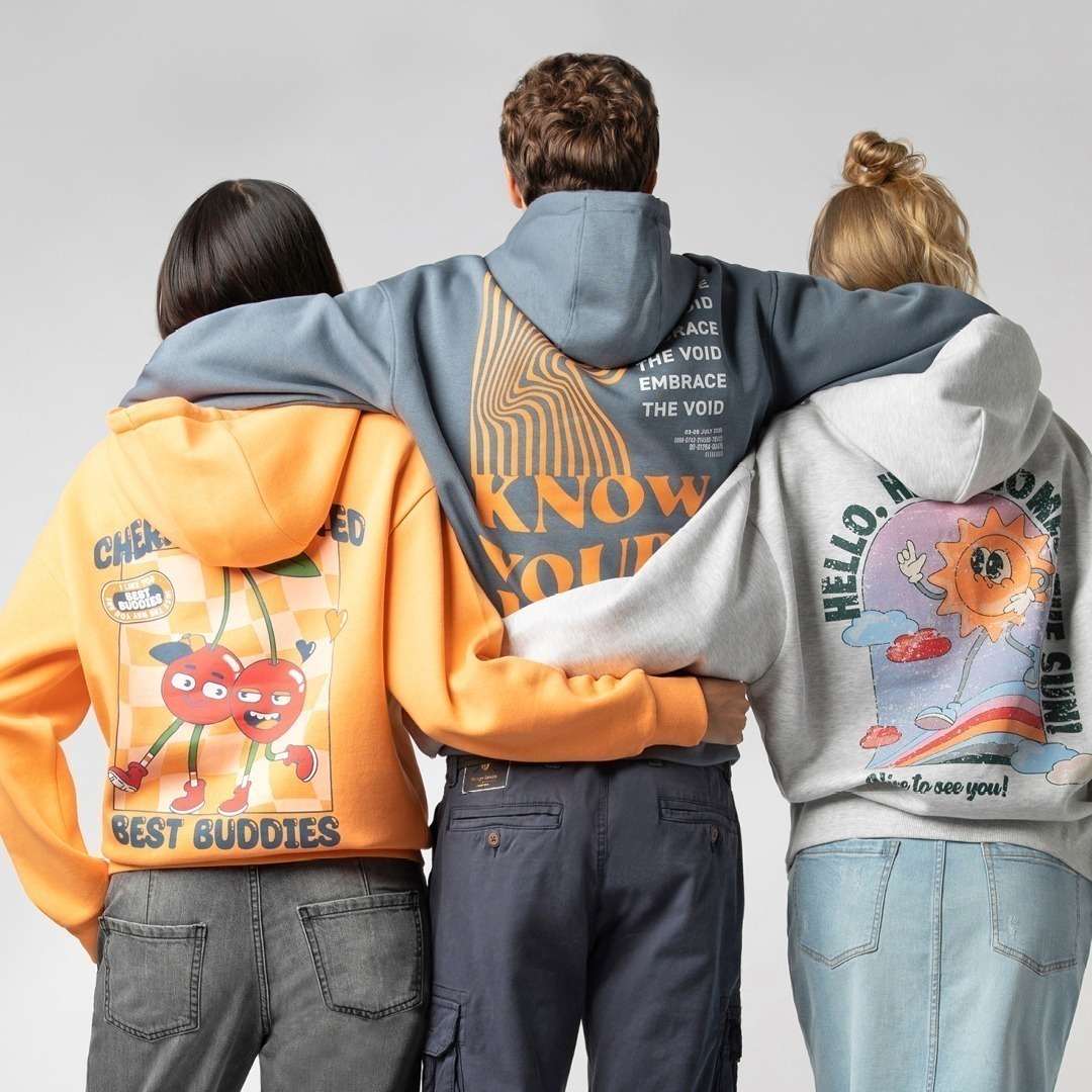 Drei Personen tragen Hoodies mit bunten Grafikdesigns auf dem Rücken: einer mit Kirschen, einer mit dem Wort „KNOW“ und einer mit einer Sonne. Drei Personen tragen Hoodies mit bunten Grafikdesigns auf dem Rücken: einer mit Kirschen, einer mit dem Wort "KNOW" und einer mit einer Sonne.