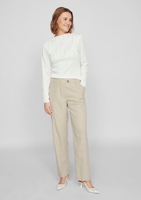 Eine lächelnde Frau trägt ein weißes Oberteil und beige Hosen sowie helle Schuhe. Eine lächelnde Frau trägt ein weißes Oberteil und beige Hosen sowie helle Schuhe.