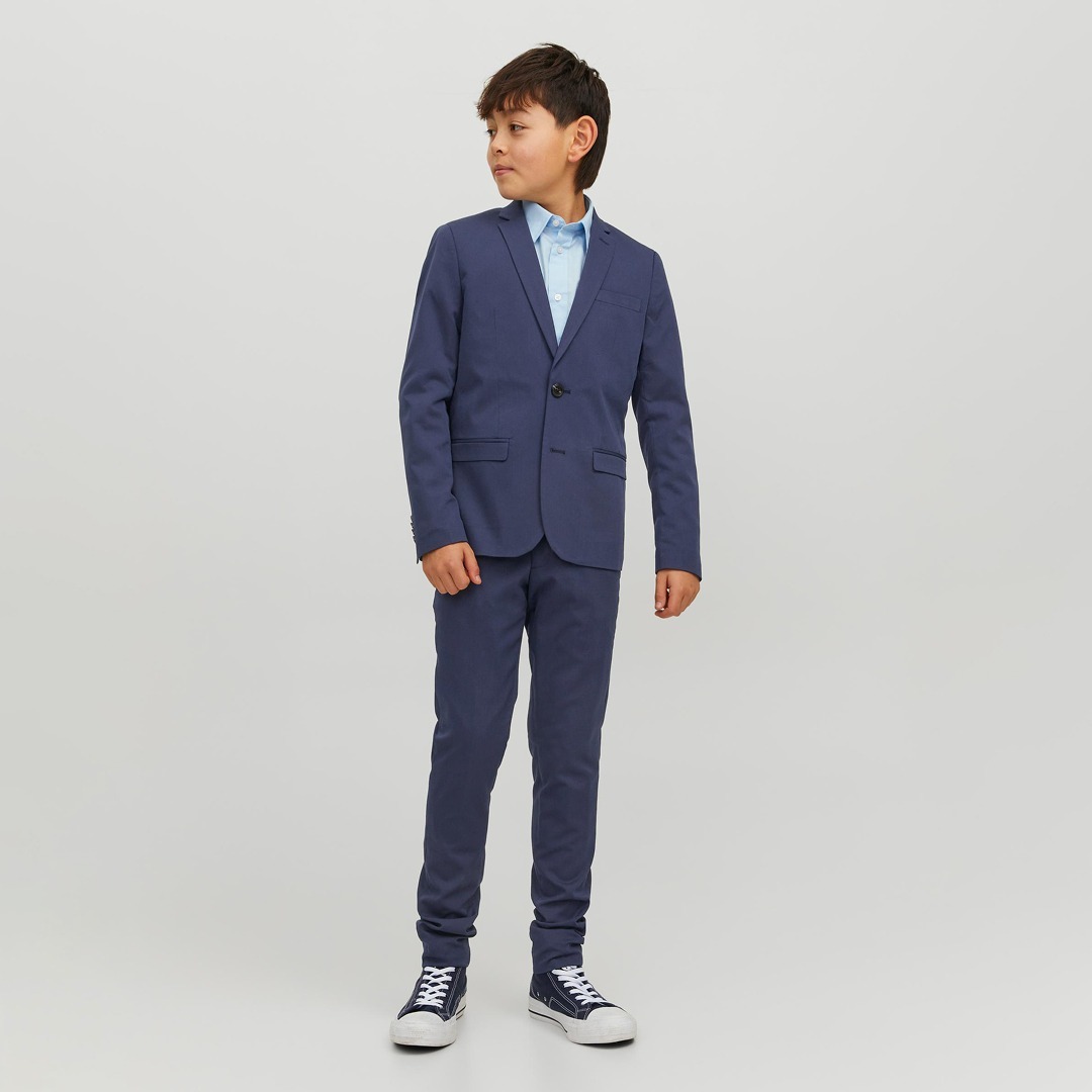Ein Junge in einem dunkelblauen Anzug mit einem hellblauen Hemd und weißen Sneakers. Ein Junge in einem dunkelblauen Anzug mit einem hellblauen Hemd und weißen Sneakers.