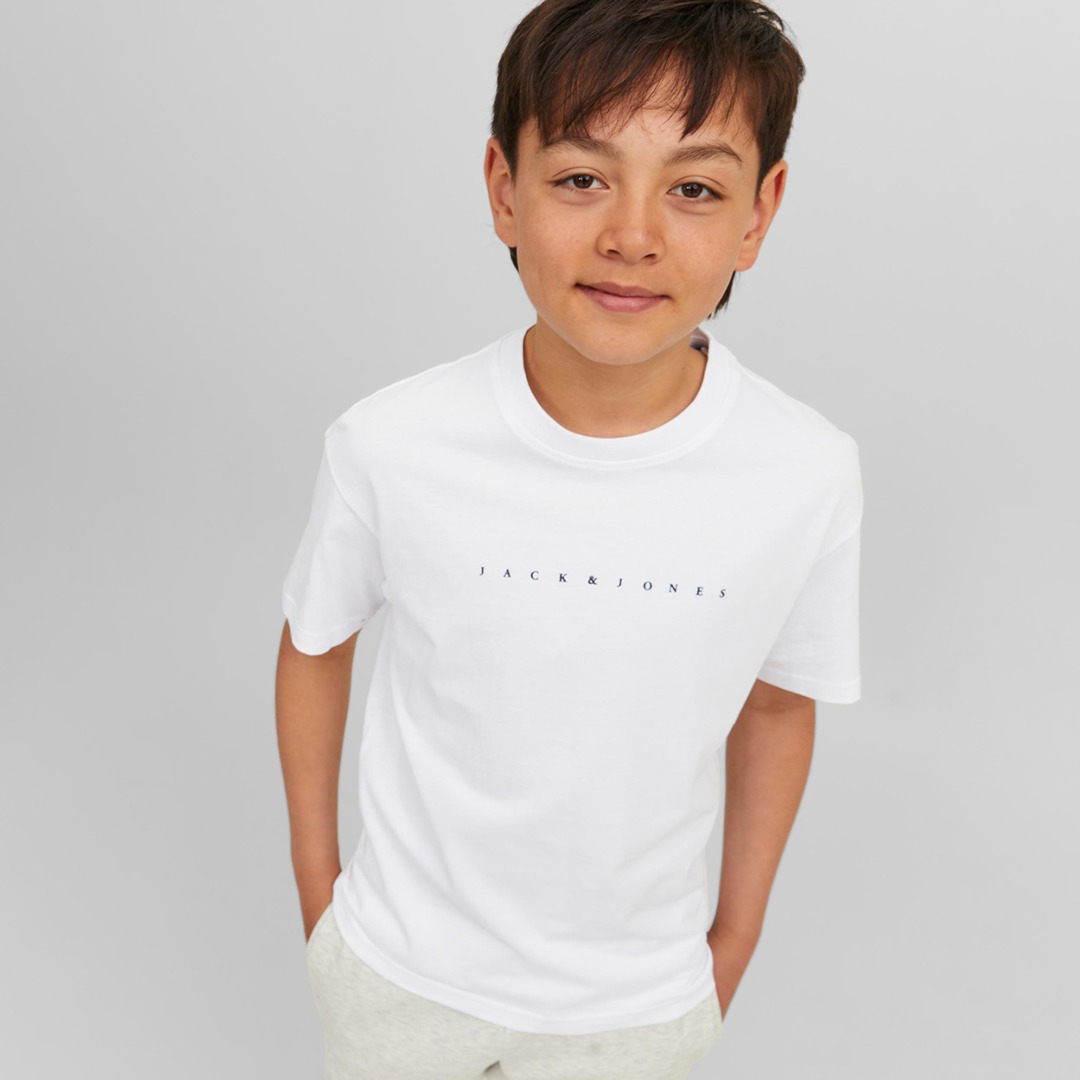 Ein Junge trägt ein weißes T-Shirt mit dem Aufdruck „JACK & JONES“ und sieht in die Kamera. Ein Junge trägt ein weißes T-Shirt mit dem Aufdruck "JACK & JONES" und sieht in die Kamera.