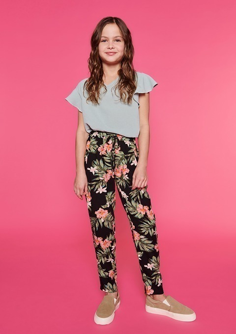 Ein Mädchen mit langen, brünetten Haaren trägt ein hellblaues Oberteil und eine schwarze Hose mit Blumenmuster. Ein Mädchen mit langen, brünetten Haaren trägt ein hellblaues Oberteil und eine schwarze Hose mit Blumenmuster.