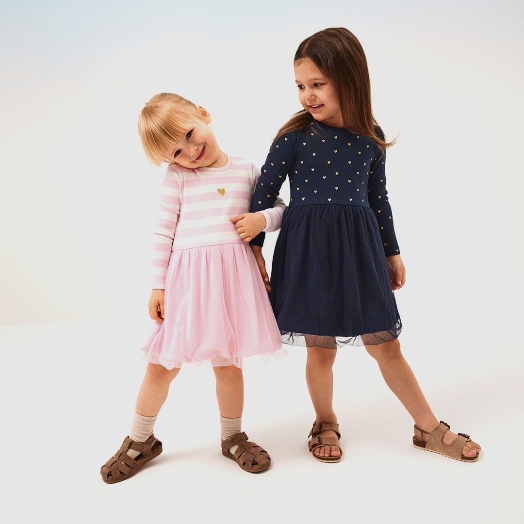 Zwei kleine Mädchen in bunten Kleidern, eines in rosa mit Streifen und das andere in marineblau mit goldenen Herzen. Zwei kleine Mädchen in bunten Kleidern, eines in rosa mit Streifen und das andere in marineblau mit goldenen Herzen.