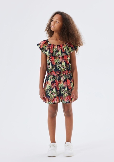 Ein Mädchen in einem bunten Kleid mit tropischem Muster steht vor einem neutralen Hintergrund. Ein Mädchen in einem bunten Kleid mit tropischem Muster steht vor einem neutralen Hintergrund.