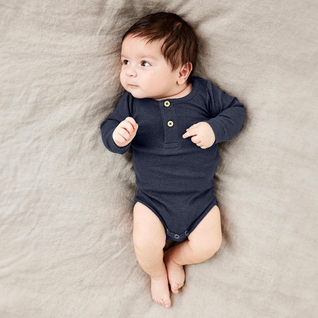 Ein Baby in einem dunkelblauen Langarmbody liegt auf einem beigefarbenen Untergrund. Ein Baby in einem dunkelblauen Langarmbody liegt auf einem beigefarbenen Untergrund.