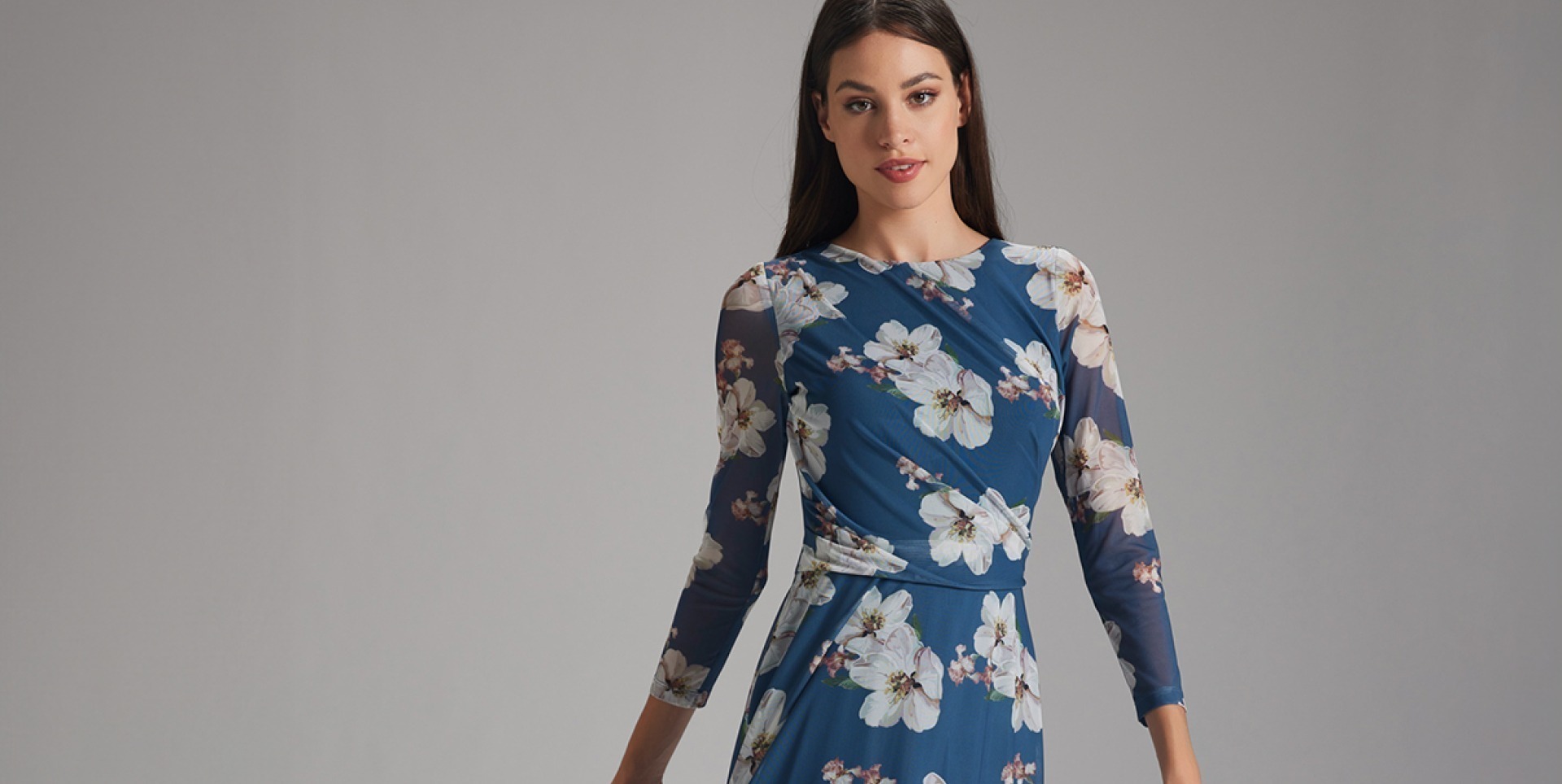 Eine Frau trägt ein elegantes, floral-musterndes Kleid in Blau mit langen Ärmeln.