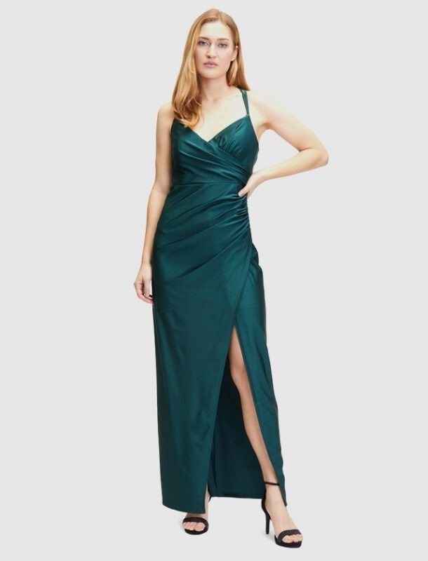 Eine Frau trägt ein elegantes, knielanges, smaragdgrünes Abendkleid mit Spaghetti-Trägern und einem hohen Schlitz.