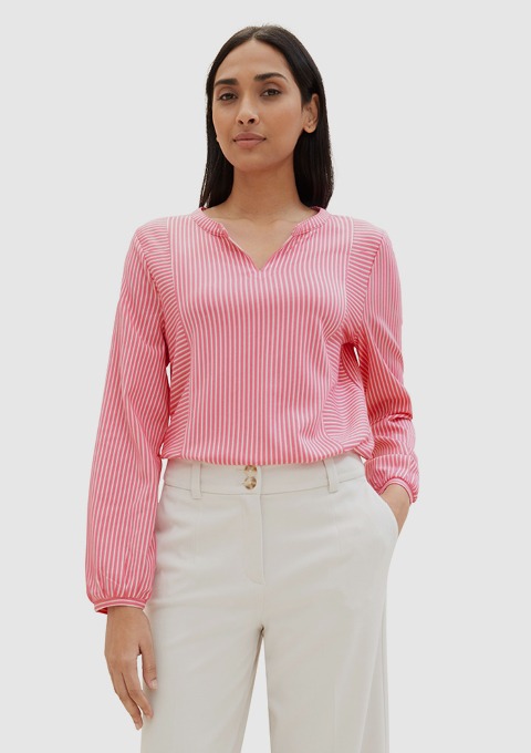 Eine Frau trägt eine langärmlige, rot-gestreifte Bluse und helle, elegante Hose. Eine Frau trägt eine langärmlige, rot-gestreifte Bluse und helle, elegante Hose.