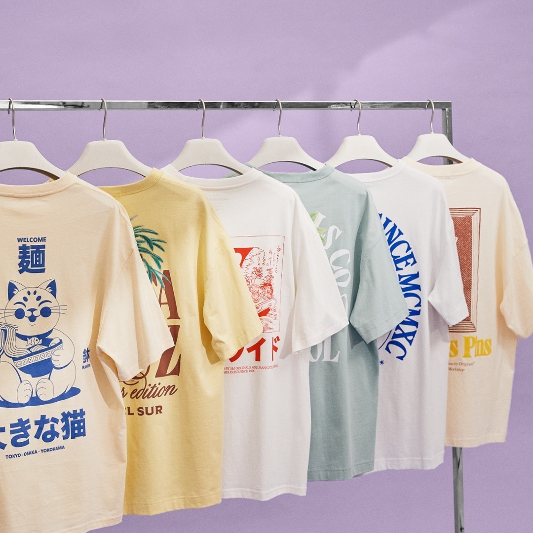 Sechs T-Shirts in verschiedenen Farben hängen an einem Kleiderbügel, vor einem lila Hintergrund.