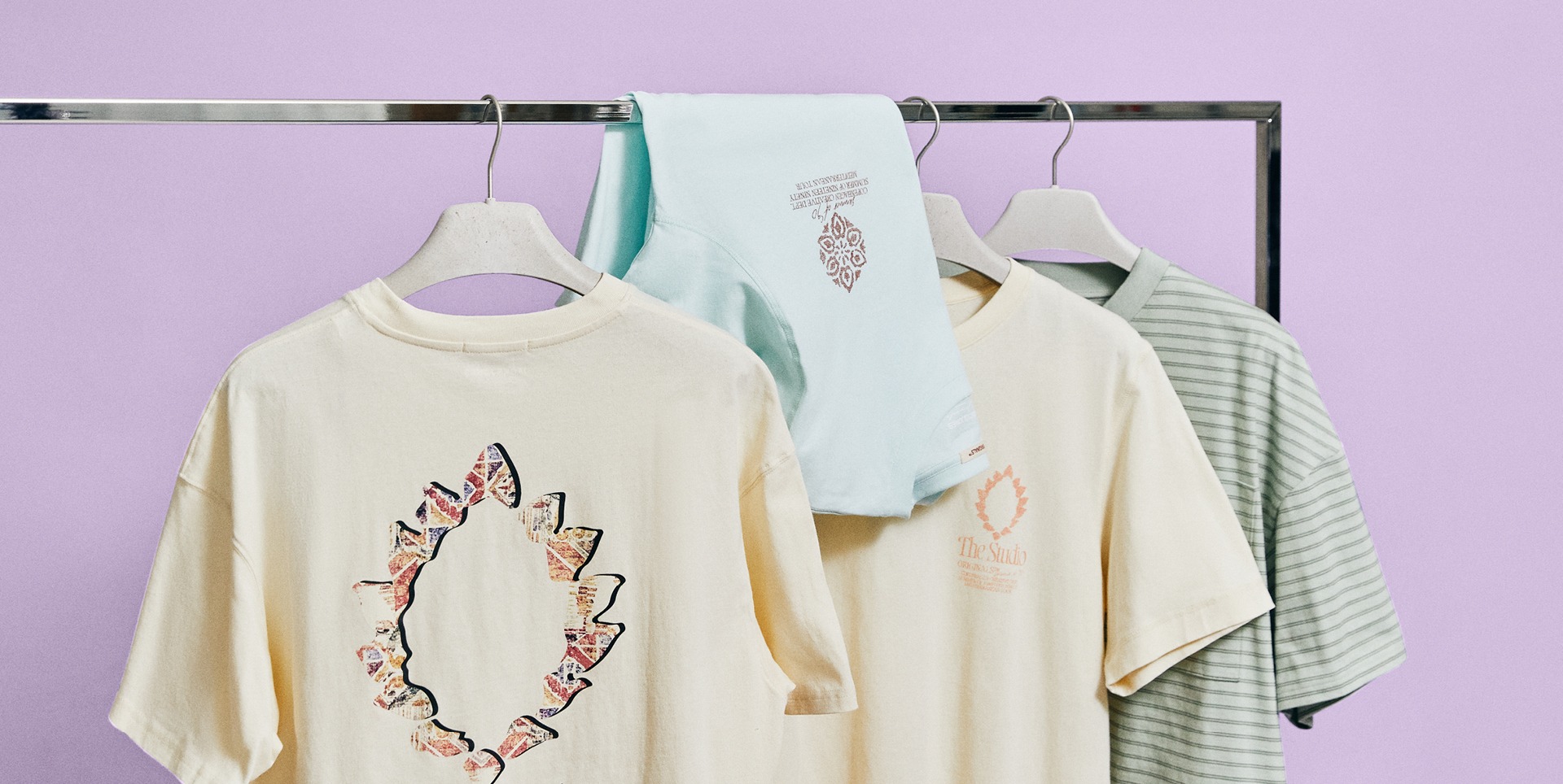 Eine Kleiderstange mit mehreren T-Shirts in verschiedenen Farben, darunter beige, mintgrün und gestreift.