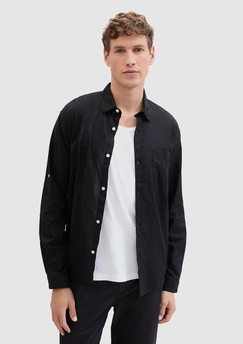 Ein Mann trägt ein schwarzes Hemd über einem weißen T-Shirt.