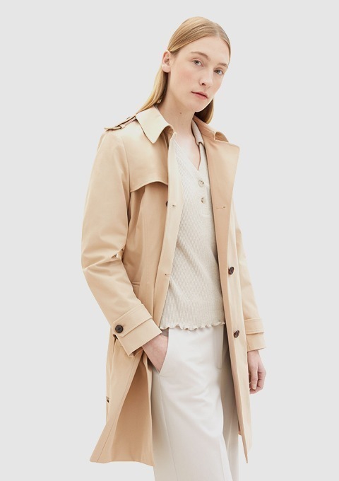 Eine Frau in einem beigen Trenchcoat mit einem weißen Oberteil und Hosen, die in einem neutralen Hintergrund posiert. Eine Frau in einem beigen Trenchcoat mit einem weißen Oberteil und Hosen, die in einem neutralen Hintergrund posiert.