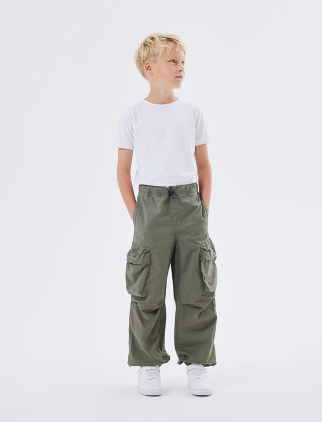 Ein Junge steht mit einem weißen T-Shirt und olivgrünen Cargo-Hosen.