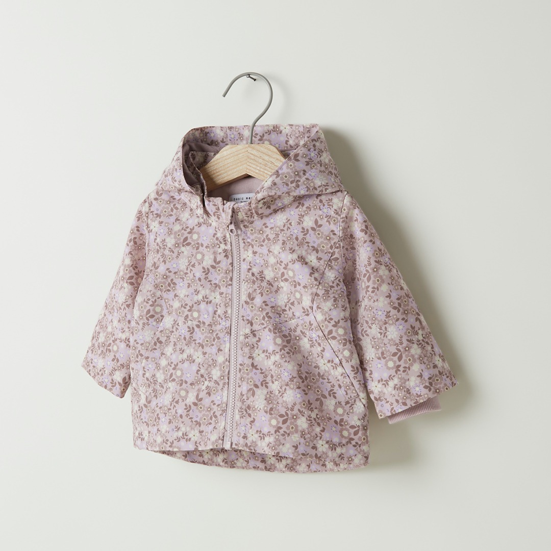 Eine rosa Jacke mit Blumendesign, an einem Holzkleiderbügel aufgehängt.
