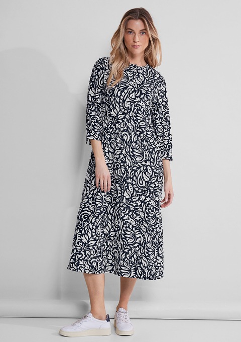 Eine Frau trägt ein langes, gemustertes Kleid in Schwarz-Weiß und weiße Sneakers. Eine Frau trägt ein langes, gemustertes Kleid in Schwarz-Weiß und weiße Sneakers.