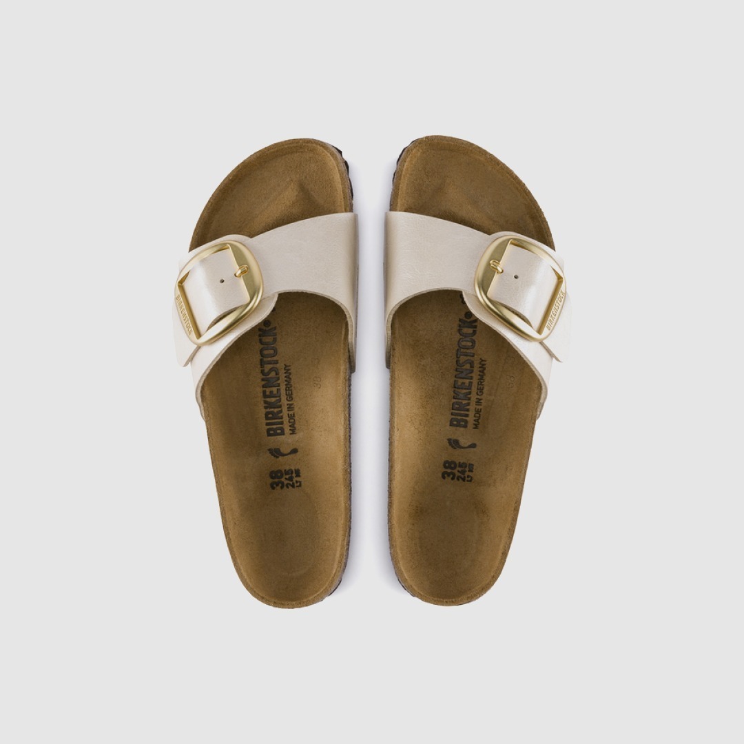 Zwei bequeme Hausschuhe von Birkenstock in hellbeige mit einer goldfarbenen Schnalle.