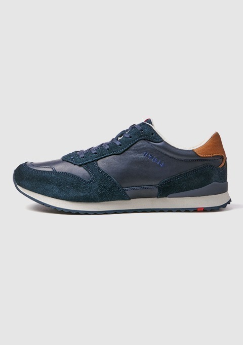 Ein dunkelblauer Sneaker mit glattem Leder und Wildleder, braunen Details und einer weißen Sohle.