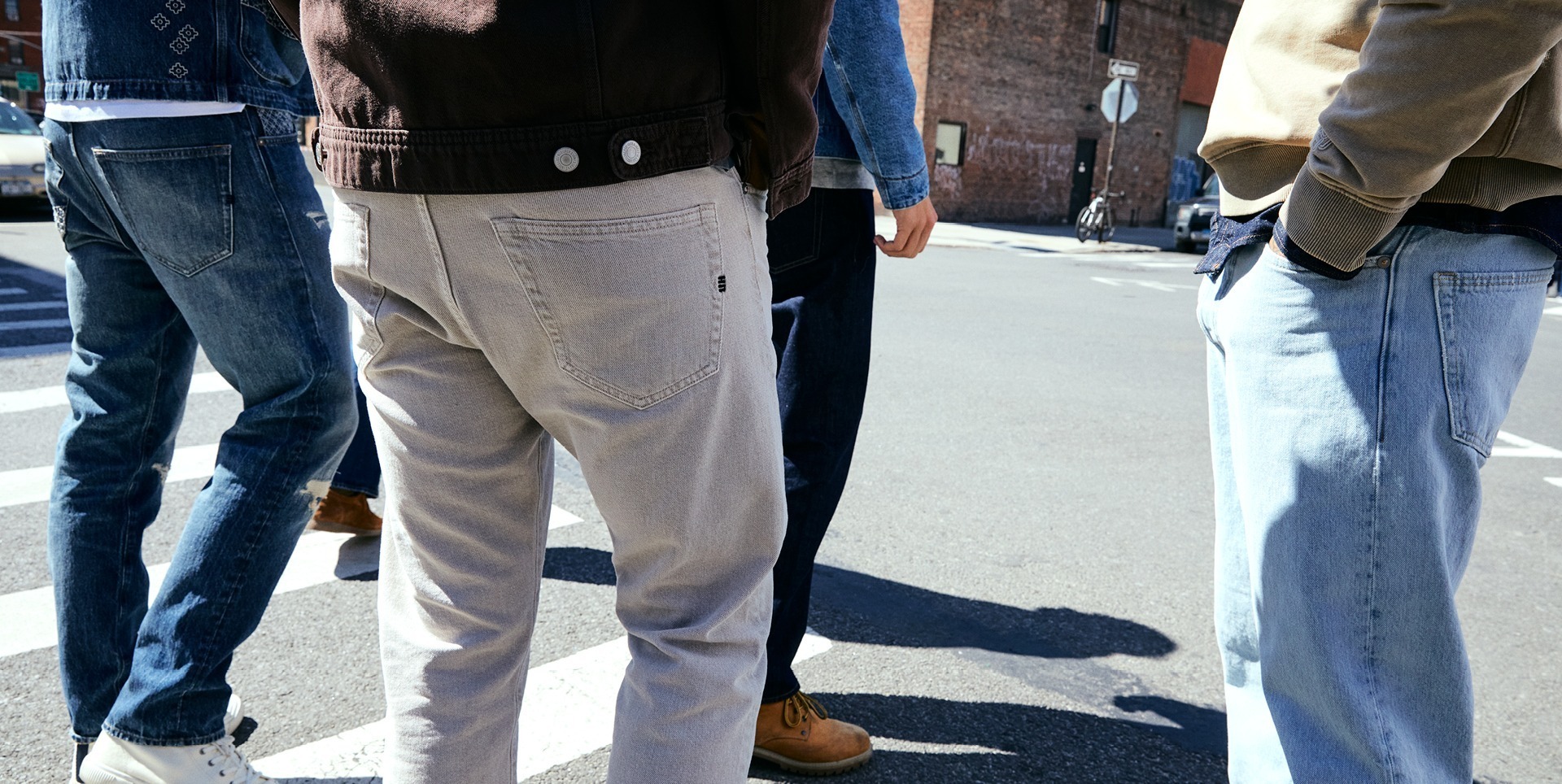 Fünf Personen stehen in einer Straßenecke, ihre Beine sind sichtbar, während sie Jeans und Chino-Hosen tragen.