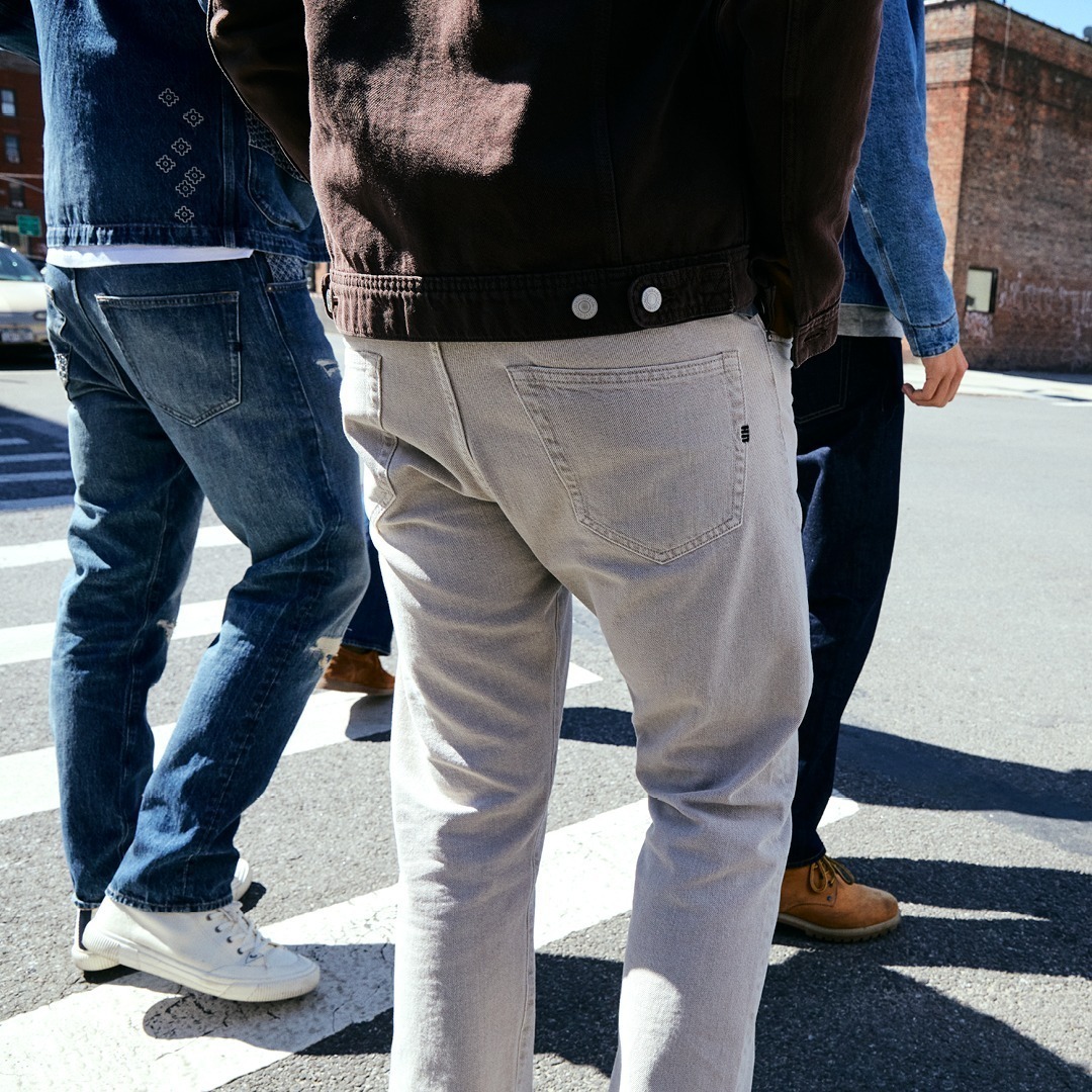 Vier Personen in Jeans und Schuhen überqueren eine Straße. Vier Personen in Jeans und Schuhen überqueren eine Straße.