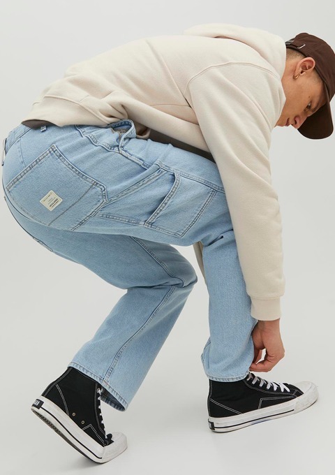 Ein Mann mit einem hellen Hoodie und einer Mütze bindet seine Schnürsenkel. Er trägt hellblaue Jeans und schwarze Sneakers. Ein Mann mit einem hellen Hoodie und einer Mütze bindet seine Schnürsenkel. Er trägt hellblaue Jeans und schwarze Sneakers.