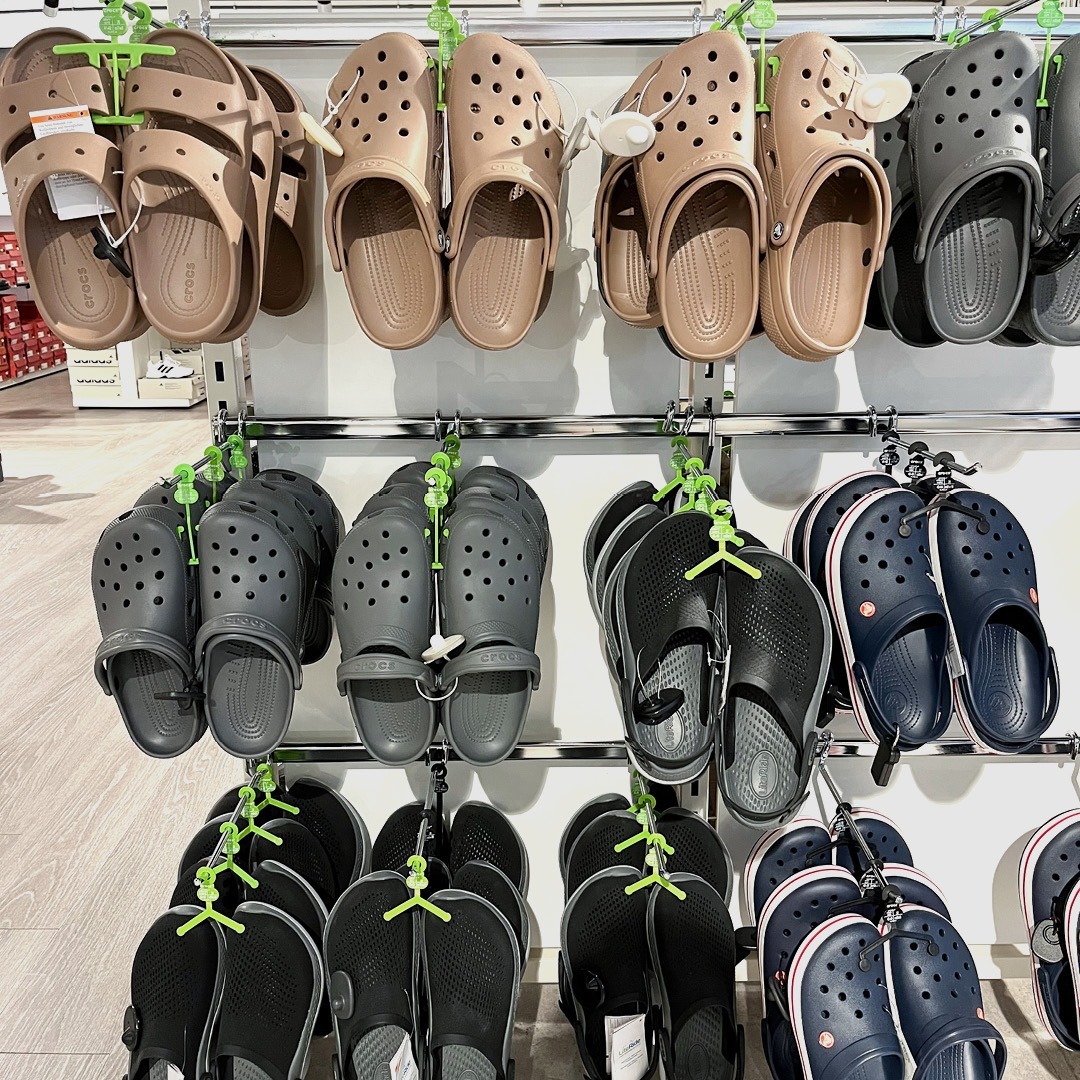 Ein Regal mit verschiedenen Crocs-Schuhen in verschiedenen Farben: braun, grau und schwarz.
