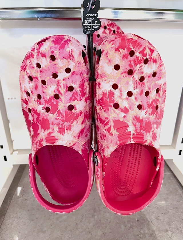 Zwei rosa Crocs mit buntem Muster, aufgehängt im Geschäft.