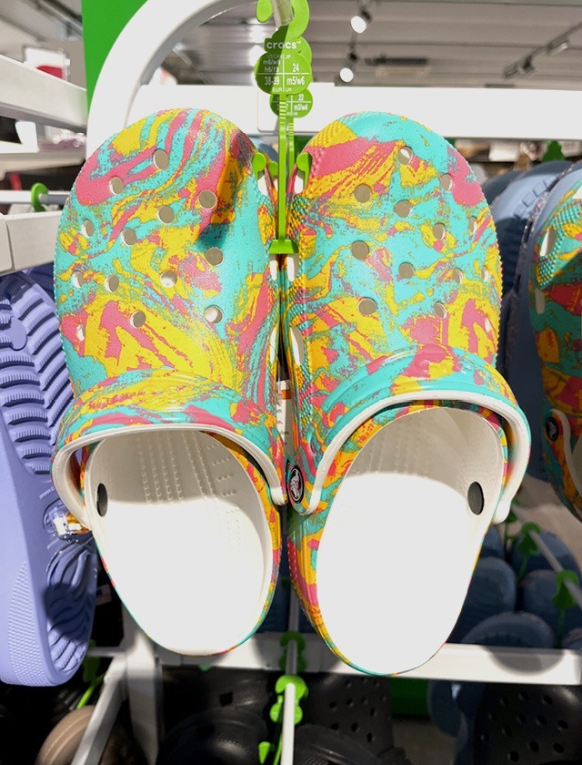 Bunte Crocs in Frühlingsdesign, aufgehängt im Verkaufsregal.