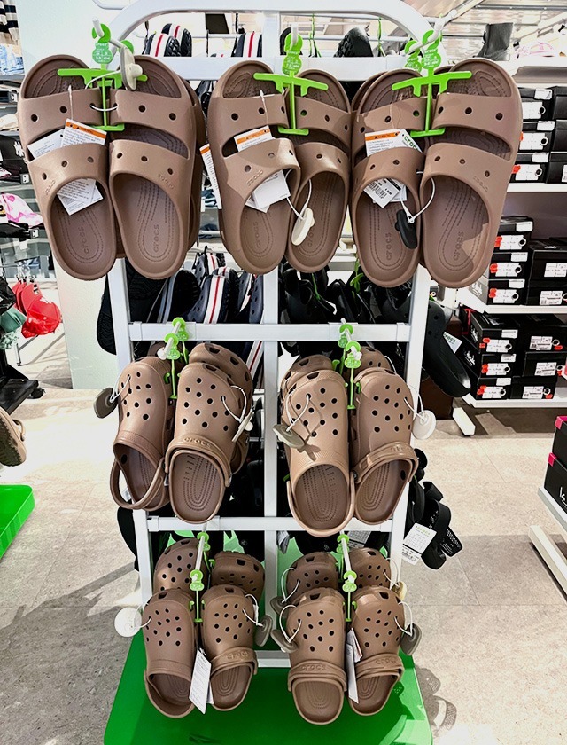 Ein Regal mit braunen Schuhen, ähnlich Crocs, in verschiedenen Größen.