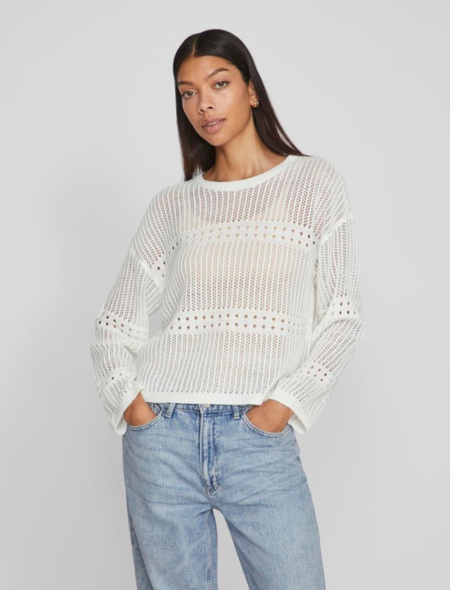 Eine Frau trägt einen weißen, nett strukturierten Pullover und eine Jeans.