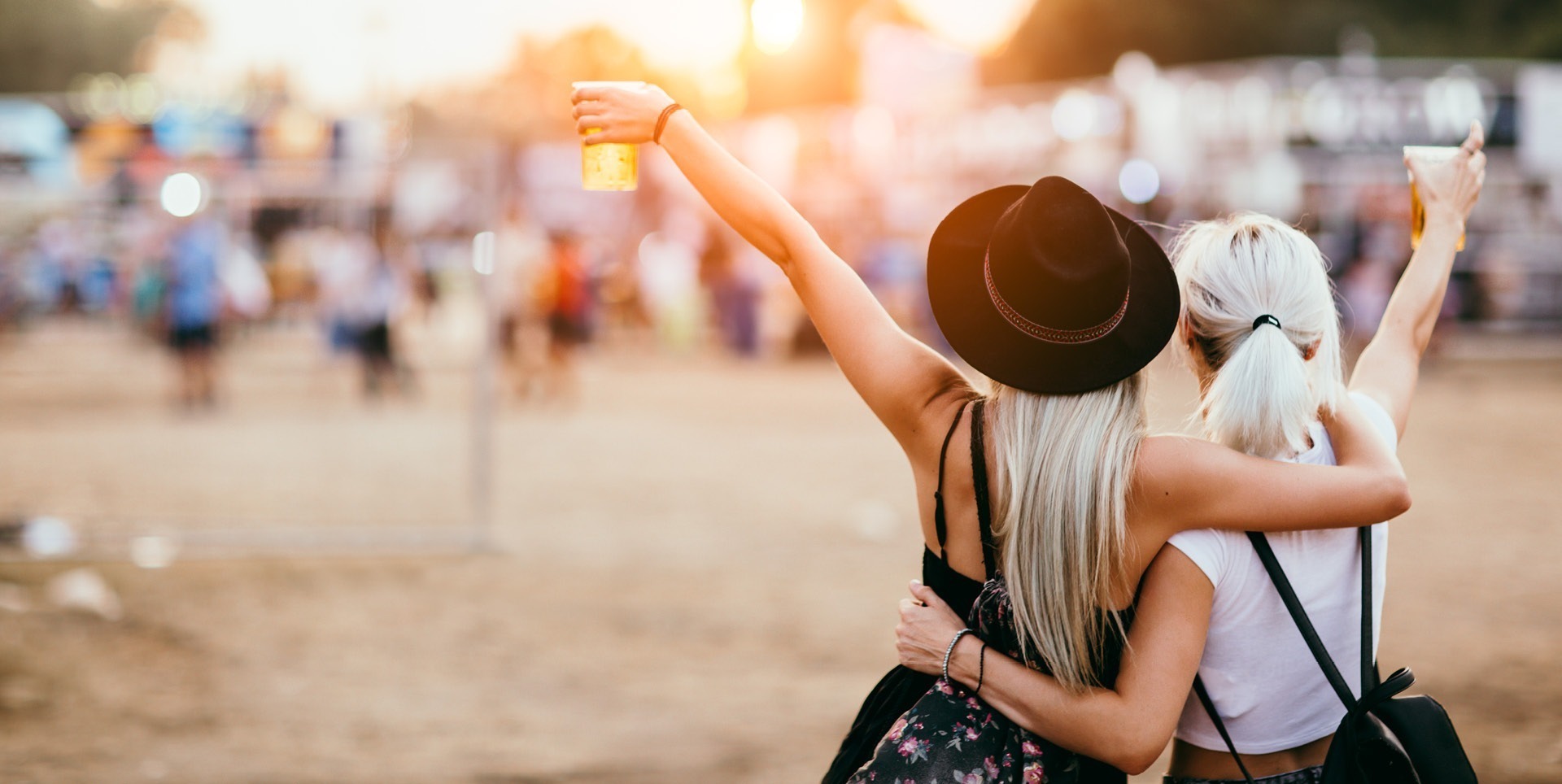 Zwei Frauen umarmen sich und heben ihre Getränke auf einem Festival im Hintergrund der Veranstaltung. Zwei Frauen umarmen sich und heben ihre Getränke auf einem Festival im Hintergrund der Veranstaltung.