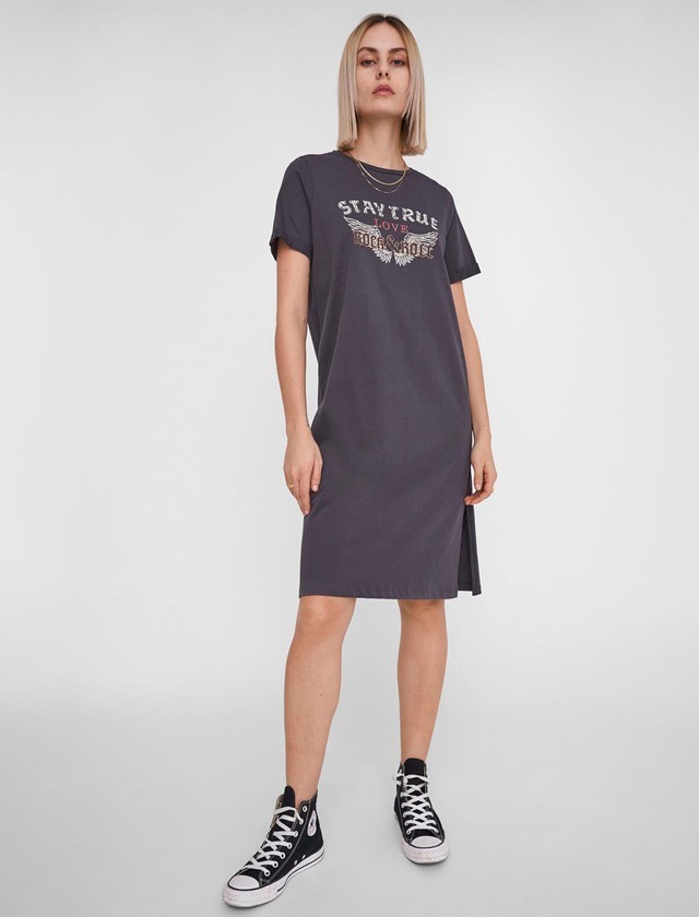 Eine Frau trägt ein graues T-Shirt-Kleid und schwarze Converse-Schuhe. Eine Frau trägt ein graues T-Shirt-Kleid und schwarze Converse-Schuhe.