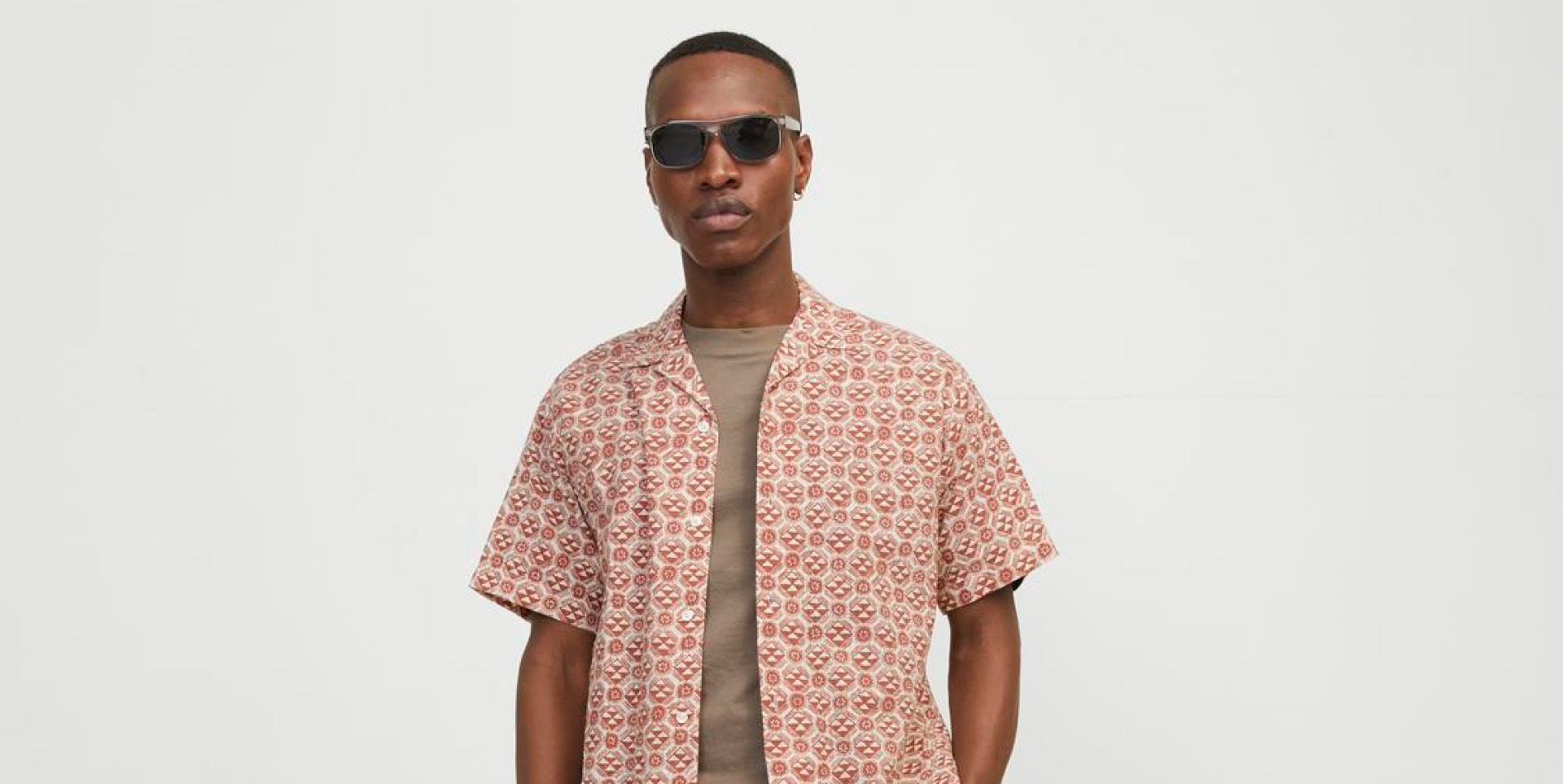 Ein Mann trägt ein gemustertes Hemd und Sonnenbrille vor einem einfarbigen Hintergrund. Ein Mann trägt ein gemustertes Hemd und Sonnenbrille vor einem einfarbigen Hintergrund.