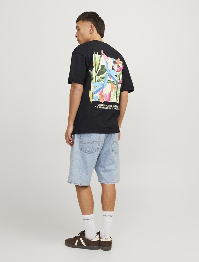 Ein Mann steht im Hintergrund, trägt ein schwarzes T-Shirt mit buntem Blumenmuster auf dem Rücken und helle Jeans-Shorts. Ein Mann steht im Hintergrund, trägt ein schwarzes T-Shirt mit buntem Blumenmuster auf dem Rücken und helle Jeans-Shorts.