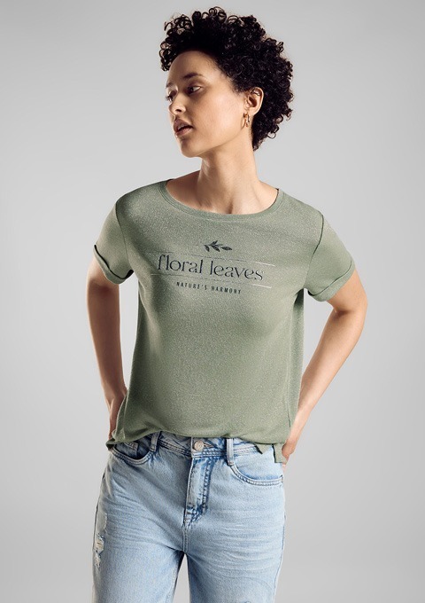 Eine Person trägt ein grünes T-Shirt mit dem Aufdruck „floral leaves“ und „NATURE’S HARMONY“ sowie blaue Jeans. Eine Person trägt ein grünes T-Shirt mit dem Aufdruck "floral leaves" und "NATURE'S HARMONY" sowie blaue Jeans.