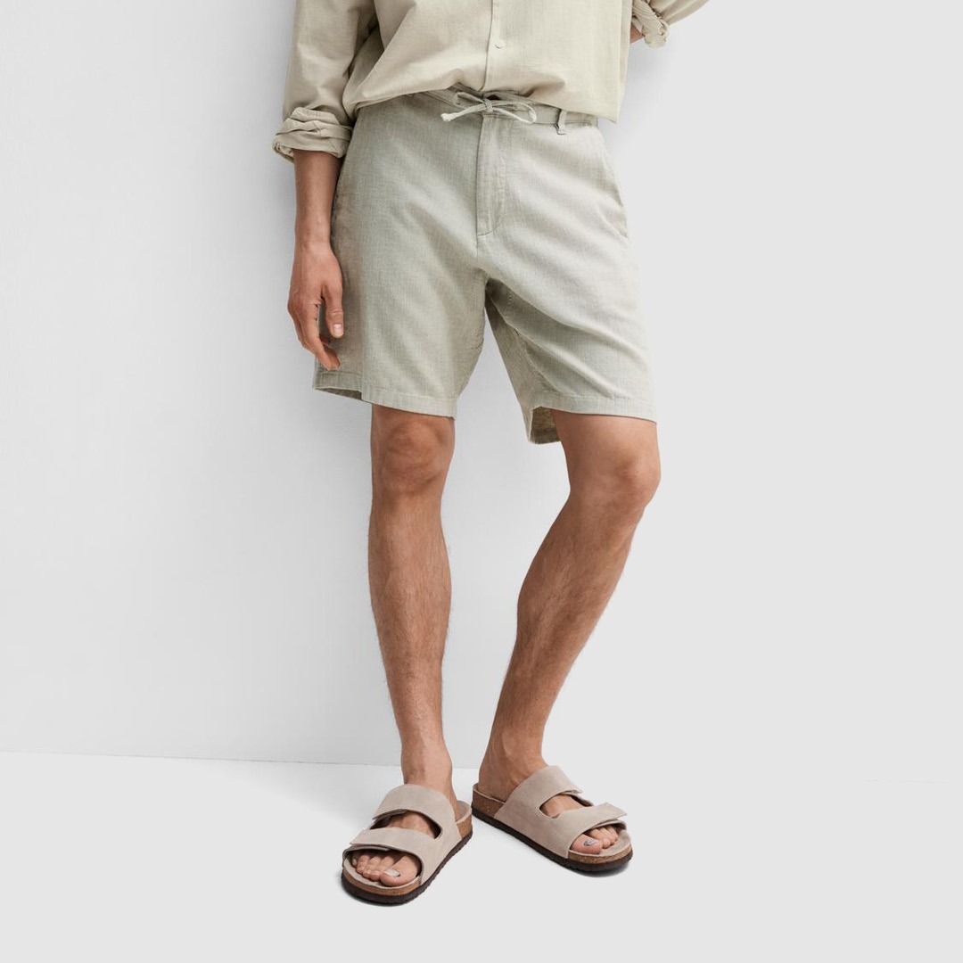 Ein Mann trägt eine lockere, helle Bluse, Shorts und Sandalen. Ein Mann trägt eine lockere, helle Bluse, Shorts und Sandalen.