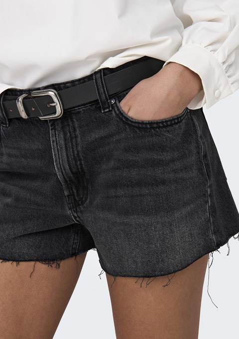 Eine Person trägt schwarze Jeansshorts mit einem Gürtel, während sie eine weiße Bluse hält.