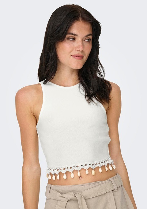 Eine Frau trägt ein ärmelloses, weißes Crop-Top mit einer Spitzenkante und Quasten.