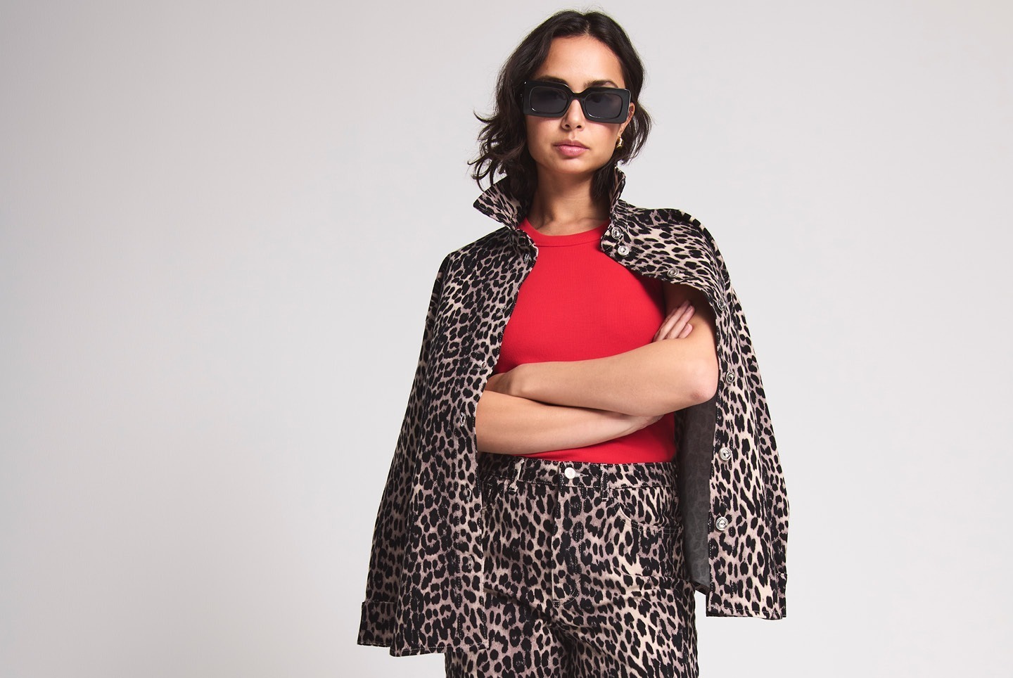 Eine Person trägt ein rotes Oberteil und eine Leopardendruck-Jacke mit passender Hose. Sie steht mit verschränkten Armen und trägt Sonnenbrillen.