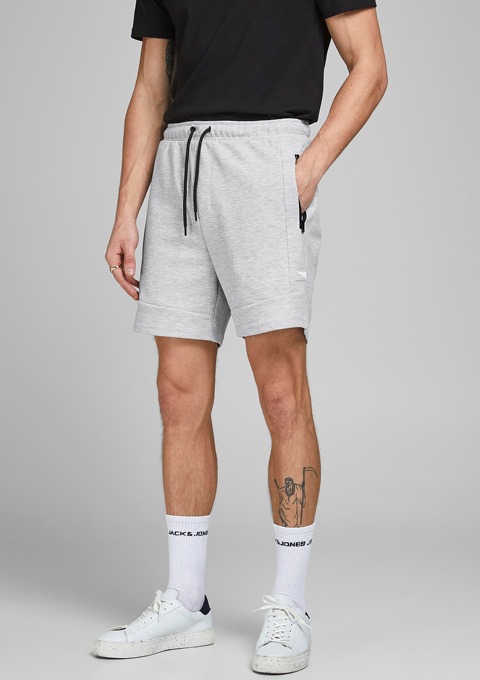 Ein Mann trägt graue Shorts, ein schwarzes T-Shirt und weiße Sneakers mit Socken.