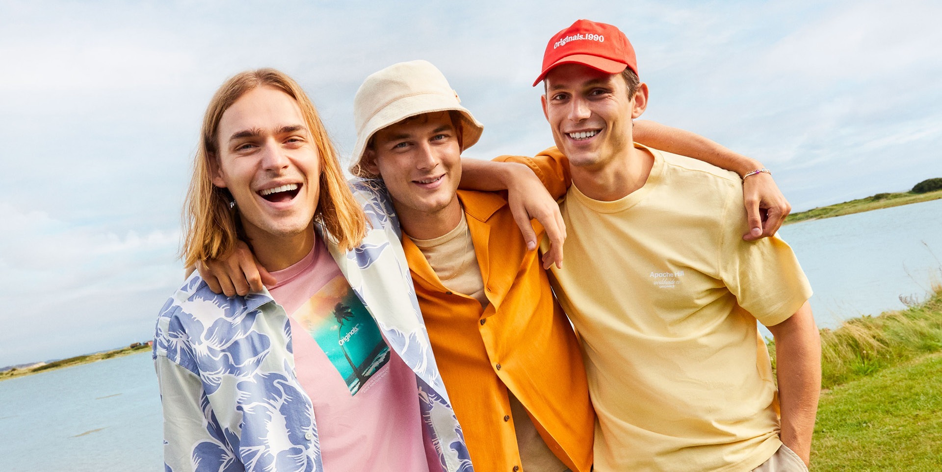 Drei junge Männer lächeln am Wasser, tragen farbenfrohe T-Shirts und sehen entspannt aus. Drei junge Männer lächeln am Wasser, tragen farbenfrohe T-Shirts und sehen entspannt aus.