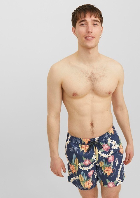 Ein shirtloser Mann trägt eine bunte Badehose mit floralem Muster.