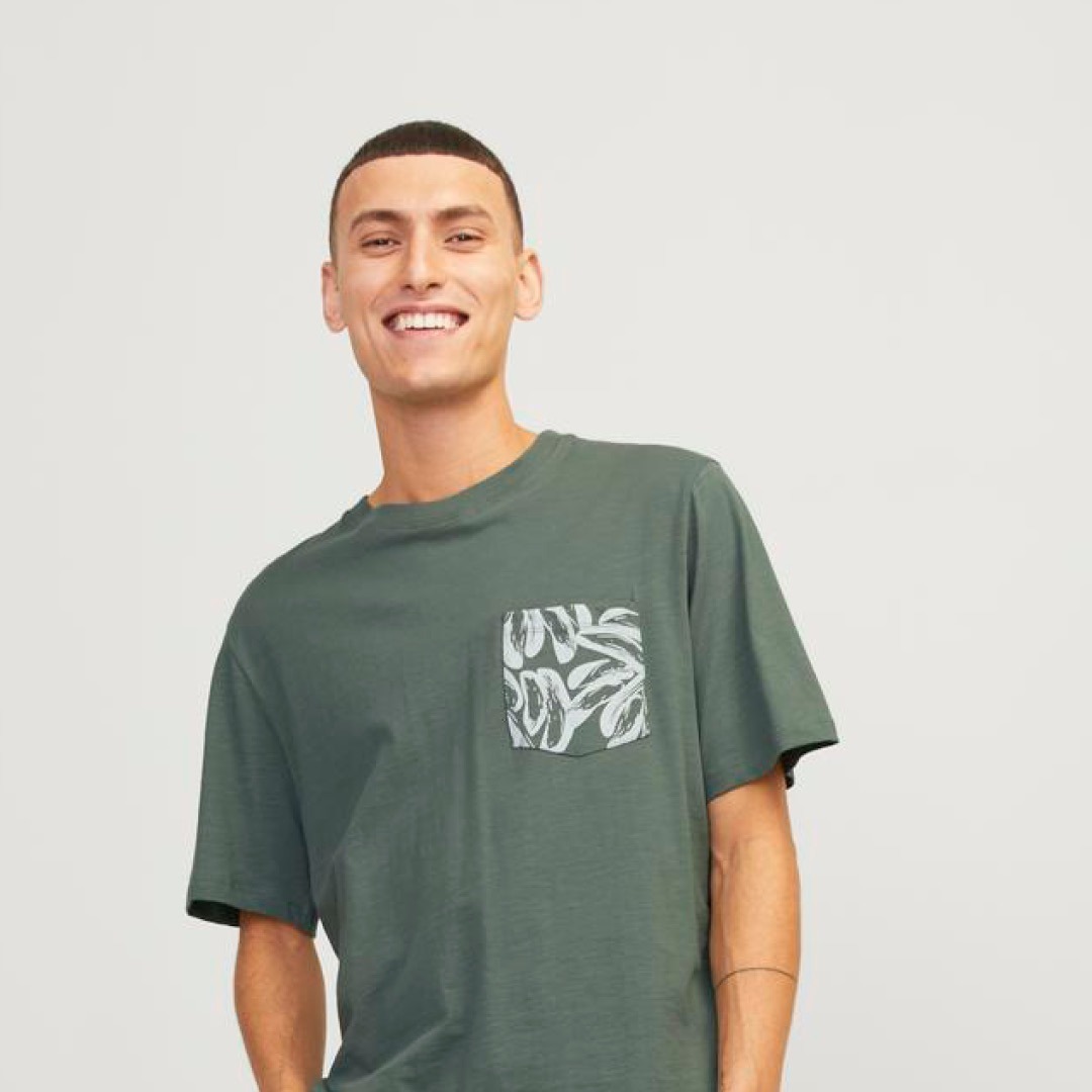 Ein Mann lächelt, trägt ein graues T-Shirt mit einer bedruckten Brusttasche. Ein Mann lächelt, trägt ein graues T-Shirt mit einer bedruckten Brusttasche.