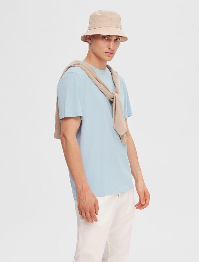 Ein junger Mann in einem hellblauen T-Shirt, mit beigem Hut und einem beigen Pullover Ăźber der Schulter. Ein junger Mann in einem hellblauen T-Shirt, mit beigem Hut und einem beigen Pullover Ăźber der Schulter.