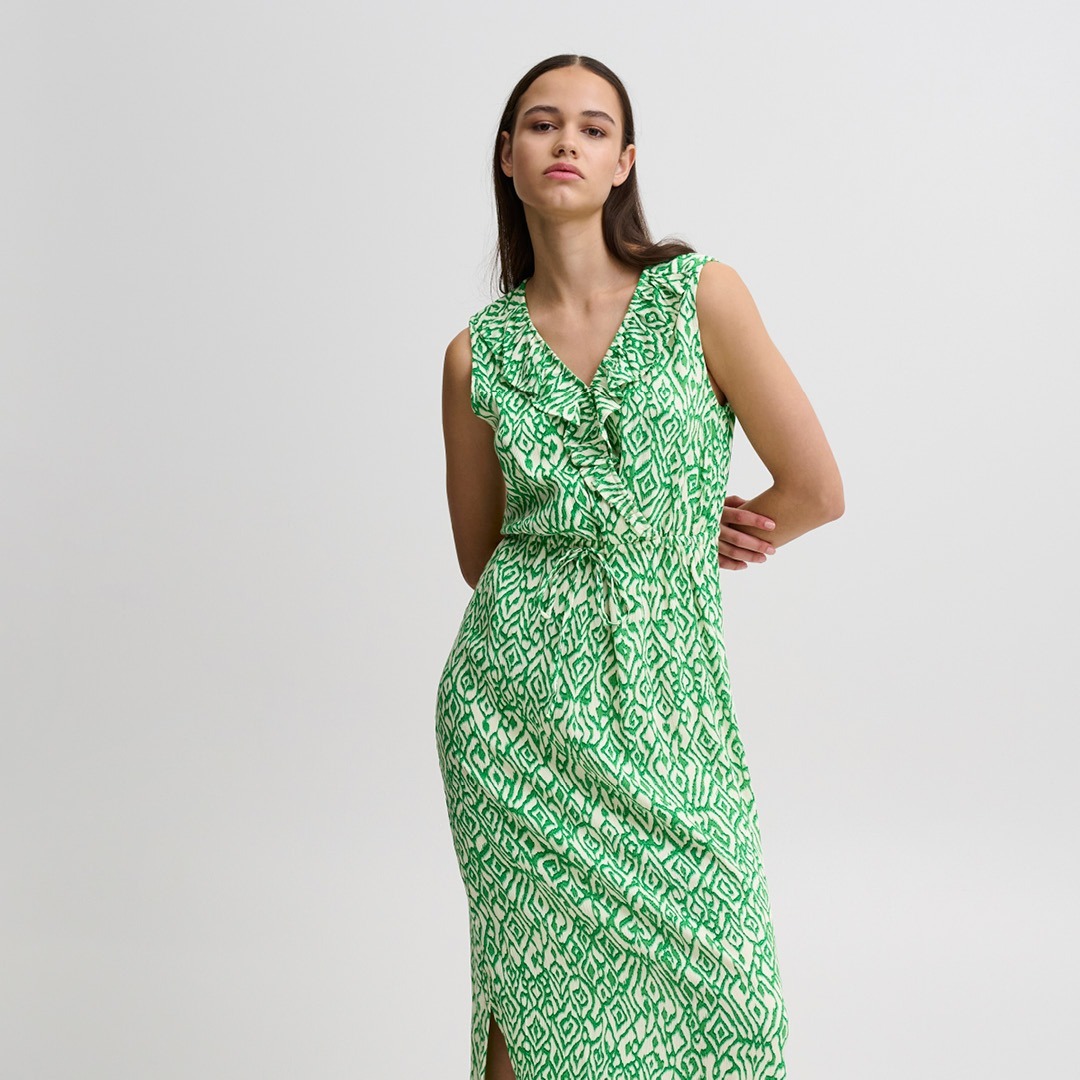 Eine Frau trägt ein ärmelloses, grßnes Kleid mit einem geometrischen Muster. Eine Frau trägt ein ärmelloses, grßnes Kleid mit einem geometrischen Muster.