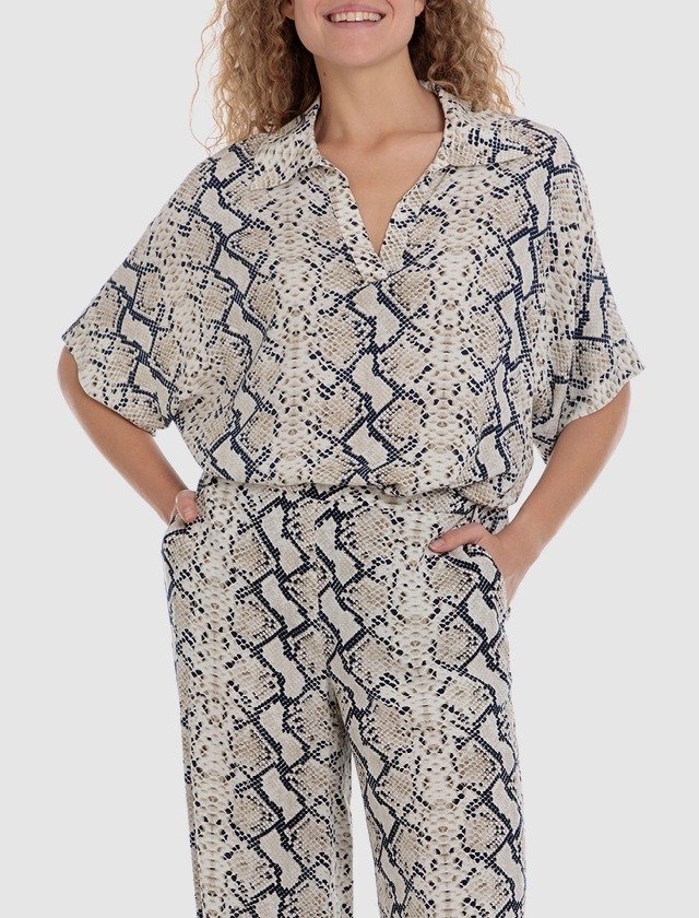 Eine Person in einem python-musternden Outfit lächelt. Sie trägt ein lockeres Oberteil mit Kragen und weite Hosen. Eine Person in einem python-musternden Outfit lächelt. Sie trägt ein lockeres Oberteil mit Kragen und weite Hosen.